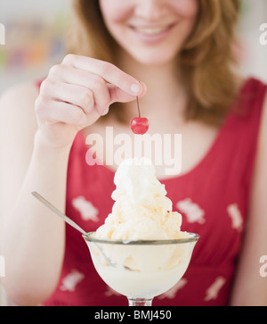 Donna mettendo una ciliegia sulla parte superiore del gelato Foto Stock