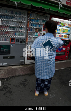 Un centro di età donna giapponese nella tradizionale festa abito sta in piedi di fronte ad una banca di distributori automatici in Asakusa Foto Stock