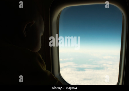 Un bambino guardando fuori della finestra in un piano Foto Stock