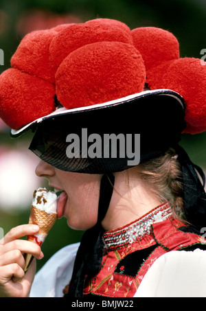 Una ragazza lecca gelato presso un festival nella Foresta Nera in Germania indossando un cappello tradizionale con pompon rosso che indica che lei è celibe. Foto Stock