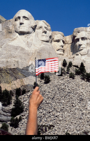 Un visitatore a Mount Rushmore National Memorial onde una bandiera americana per salutare quattro U.S. Presidenti scolpiti sul versante di una montagna in Sud Dakota, Stati Uniti d'America. Foto Stock