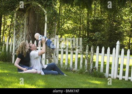 Coppia giovane e il bambino al di fuori nel prato accanto a un bianco Picket Fence Foto Stock