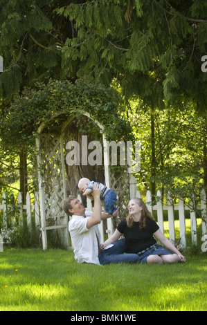 Coppia giovane e il bambino al di fuori nel prato accanto a un bianco Picket Fence Foto Stock