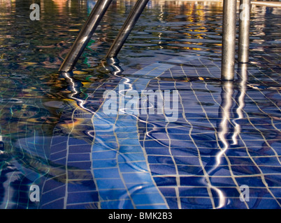 Riflessioni in acqua e una scala da uno a bordo piscina Foto Stock