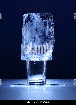 Un vetro trasparente con un piccolo blocco congelato di ghiaccio su una superficie di metallo Foto Stock