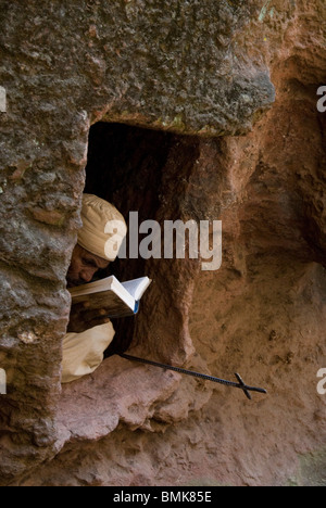 Etiopia: Lalibela, Blue Nile River Basin, monaco con croce astile leggere la Bibbia nella parete al di fuori di Beta Golgota Chiesa Foto Stock