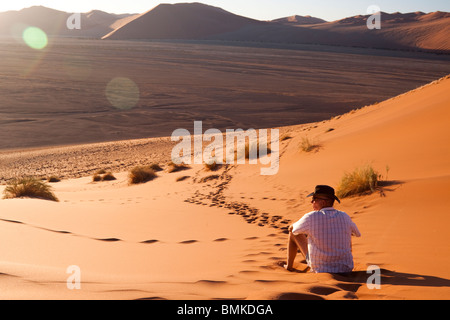 L'uomo a guardare il sole andare giù su di una duna di sabbia Foto Stock