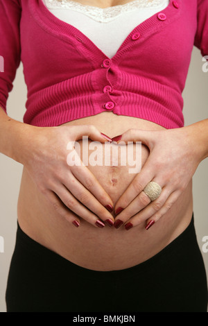 La gravidanza di una madre facendo a forma di cuore con le mani sul suo stomaco Foto Stock