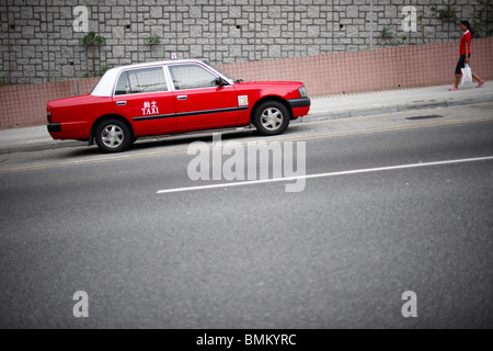 Un rosso taxi parcheggiato su un terreno in pendenza con un abito pedonale nella stessa colpendo red camminando verso la vettura, trasportare bianco sacchetto di plastica. Foto Stock