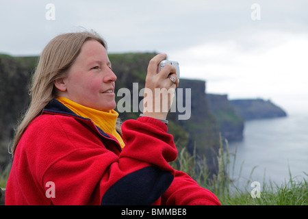 Giovane donna prendendo fotografie delle scogliere di Moher, Co. Clare, Repubblica di Irlanda Foto Stock