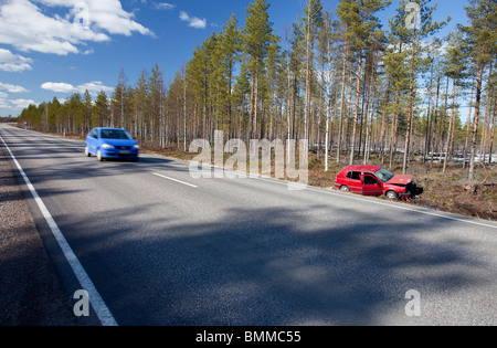 Auto blu che passa da un crash Volkswagen Golf rosso posa a bordo strada fossato, Finlandia Foto Stock