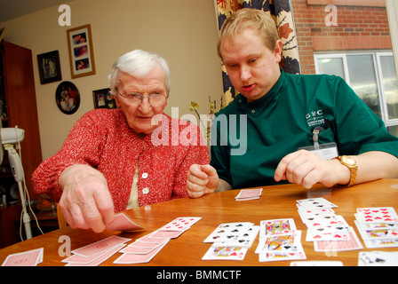 Lavoratore di cura giocando a carte con una signora anziana in assistenza residenziale home, Wirral, Regno Unito. Foto Stock