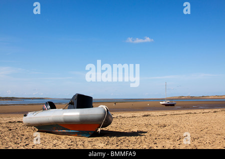 Una piccola barca che si siede sulla sabbia sulla spiaggia instow in una giornata di sole con uno yacht in background e una persona a piedi un cane Foto Stock