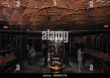 Gli operatori con torcia soffiante e il palo di legno di illuminazione e di sollevamento di coni di incenso interno del Tempio di Man Mo, Sheung Wan, Hong Kong Foto Stock