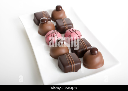 Varietà di deliziosi cioccolatini sul lungo piatto di vetro con sfondo bianco. Foto Stock