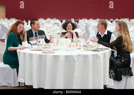 Cinque giovani al bianco rotondo tavolo nel ristorante. Cena di gala Foto Stock