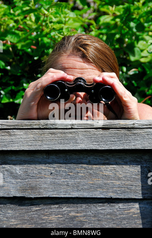 Una donna ficcanaso a spiare i suoi vicini di casa. Foto Stock