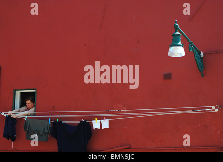 Una donna si blocca un lavaggio su una linea di abbigliamento per il suo dipinto luminosamente house, Burano, Italia Foto Stock