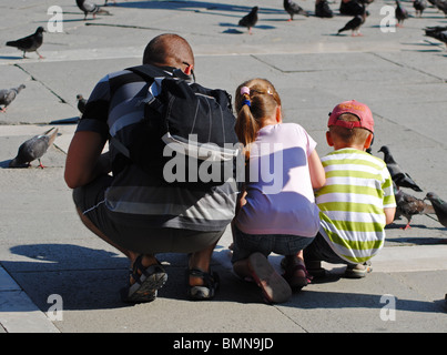 Un padre e i suoi figli feed i piccioni in Piazza San Marco, Venezia, Italia Foto Stock