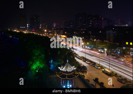 Sentieri di luce dai fari degli autoveicoli acquisiti su una strada principale molto trafficata in Changsha city, nella provincia del Hunan, Cina, contro la silhouette della città. Foto Stock