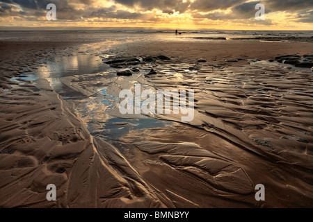 Silhouette di un uomo a piedi il suo cane al tramonto lungo le rive del Dunraven Bay nel Galles del Sud Foto Stock