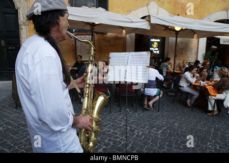 Un uomo di riprodurre musica sassofono nella strada di fronte ristorante roma italia i turisti di mangiare la cena. Foto Stock