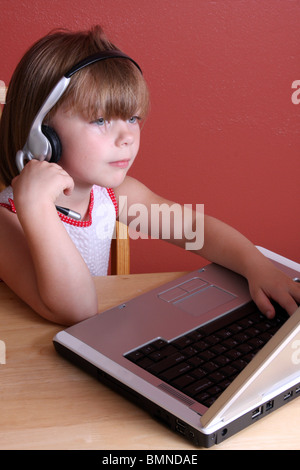 Una giovane ragazza parlando su un auricolare e al lavoro su un notebook business bambini Foto Stock