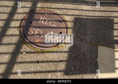 Chiusino in New York con un segno di fognature di NYC. Posizionamento del coperchio assomiglia a una bandiera con strisce Foto Stock