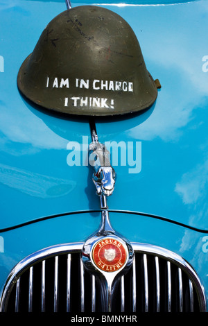 Un vecchio casco vintage sul cofano di una Jaguar auto con una Jaguar argento ornamenti del cofano Foto Stock