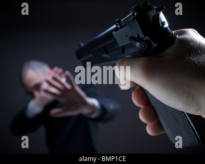 Una minacciosa mano indicando una pistola su un inerme indifeso di imprenditore. Foto Stock