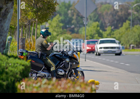 Cercando di catturarne speeders, un motociclo poliziotto prepara un accelerando la citazione sul suo quaderno come veicoli che sopraggiungono in senso contrario si avvicina Foto Stock