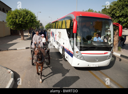 Un moderno pullman turistico passa i turisti in un tradizionale cavallo e carrozza (Hantoor), Luxor, l'Alto Egitto Foto Stock