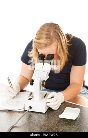 Teen girl nella classe di scienze guarda attraverso il microscopio e scrive le sue osservazioni. Sfondo bianco. Foto Stock