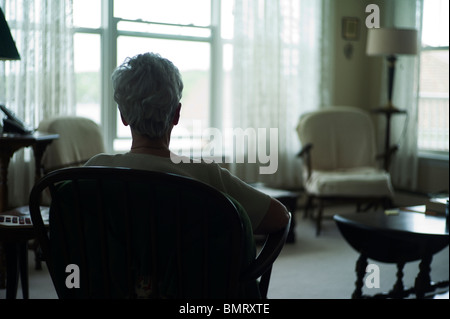 Vecchia donna da dietro come si siede a guardare fuori dalla finestra. Foto Stock