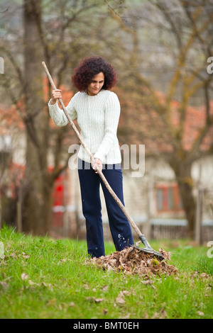 Giovani redhead pretty country girl utilizzando un rastrello per ripulire la caduta foglie Foto Stock