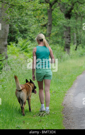 Donna con un belga cane pastore camminando sul ciglio della strada nella campagna del Berkshire England Regno Unito Foto Stock