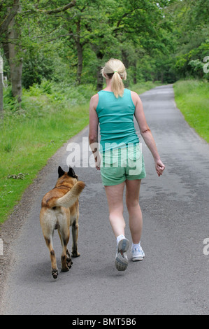 Donna con un belga cane pastore camminando sul ciglio della strada nella campagna del Berkshire England Regno Unito Foto Stock