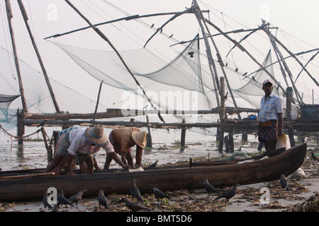 I pescatori con la loro barca vicino cinese reti da pesca al Fort Kochi (Cochin) spiaggia in Kerala, India. Foto Stock