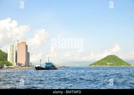 Cielo blu vista mare di Isola Verde e carichi pericolosi rimorchiatore avvicinando Kennedy Town, West End Victoria Harbour, Hong Kong Foto Stock