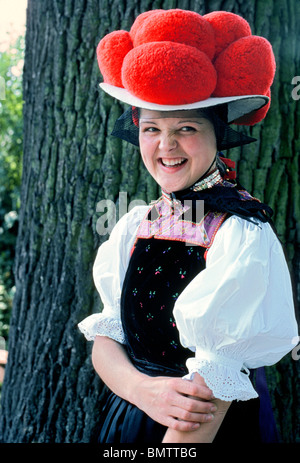 Un sorridente ragazza tedesca a un festival culturale nella Foresta Nera in Germania indossa un cappello tradizionale con pompon rosso che indica che lei è celibe. Foto Stock