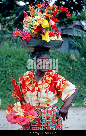 Un fiore coloratissimo fornitore che equilibra la maggior parte dei fiori sul suo capo accoglie i visitatori per l'isola francese della Martinica. Foto Stock
