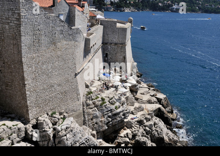 Ai turisti di rilassarsi con un drink sulle rocce sotto le ripide mura della città di Dubrovnik Foto Stock