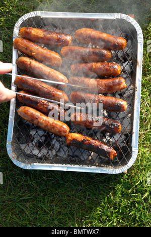 Salsicce su un barbecue monouso Foto Stock