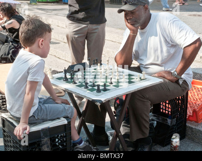 Adulto Uomo nero & piccolo ragazzo caucasico seduto su rovesciato cassette in plastica impegnarsi in un serio gioco di scacchi in Union Square NYC Foto Stock