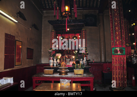 Signora cinese pregare presso un santuario, con joss bastoni e divinità taoista, in una stanza laterale del Tempio di Man Mo, Sheung Wan, Hong Kong Foto Stock