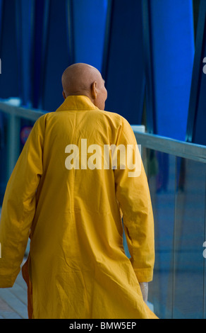 Un monaco buddista in un giallo brillante impermeabile passeggiate sul lungomare vicino al traghetto Star di Hong Kong il quartiere centrale. Foto Stock