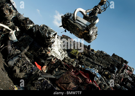 Rottami di gru di cantiere con auto schiacciata con altri frantumato vetture demolite in pila. Foto Stock