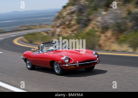 Un rosso brillante 1969 Jaguar E-type Roadster accelera attraverso una curva in salita - motion è sottolineato dal panning. Foto Stock