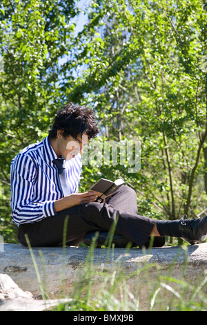 Giovane uomo in abito di business, la lettura (Shakespeare) nel parco Foto Stock