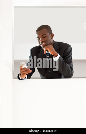 I giovani adulti afro-imprenditore americano la lettura dei messaggi di posta elettronica sul suo smartphone all'interno. Spazio di copia Foto Stock